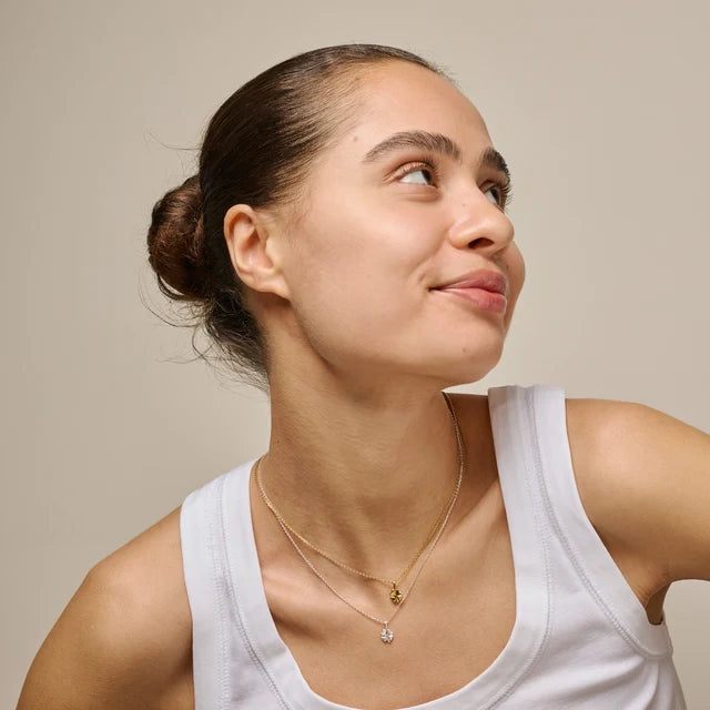 Woman wearing a white tank top and gold necklaces against a beige background