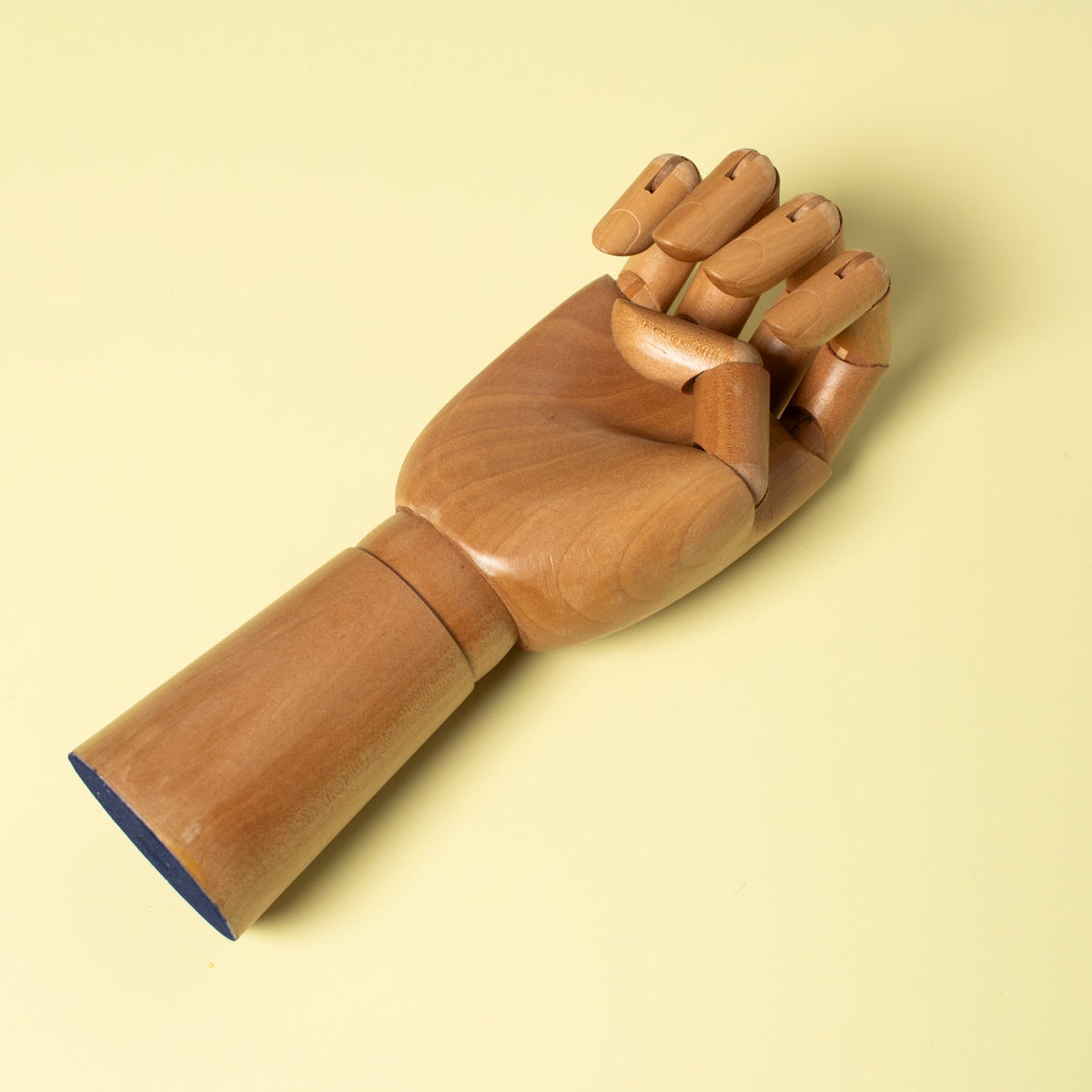 A wooden articulated hand model with a closed fist, shown on a solid pale yellow background.