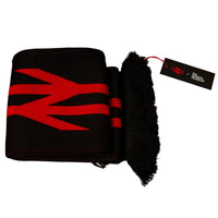 A folded black knit scarf with a bold red geometric logo pattern, featuring a fringed edge and a black hangtag, set against a solid red background.