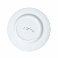 A white ceramic plate photographed from above on a light wood-grain surface, with the printed text 'Es Devlin 700' in the center.