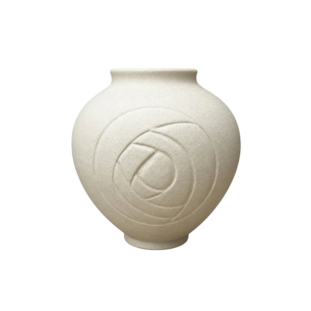 A small matte ceramic vase with a rounded bulbous body, short flared rim, and an embossed circular floral motif on the front, shown on a light wood surface against a gray textured wall.