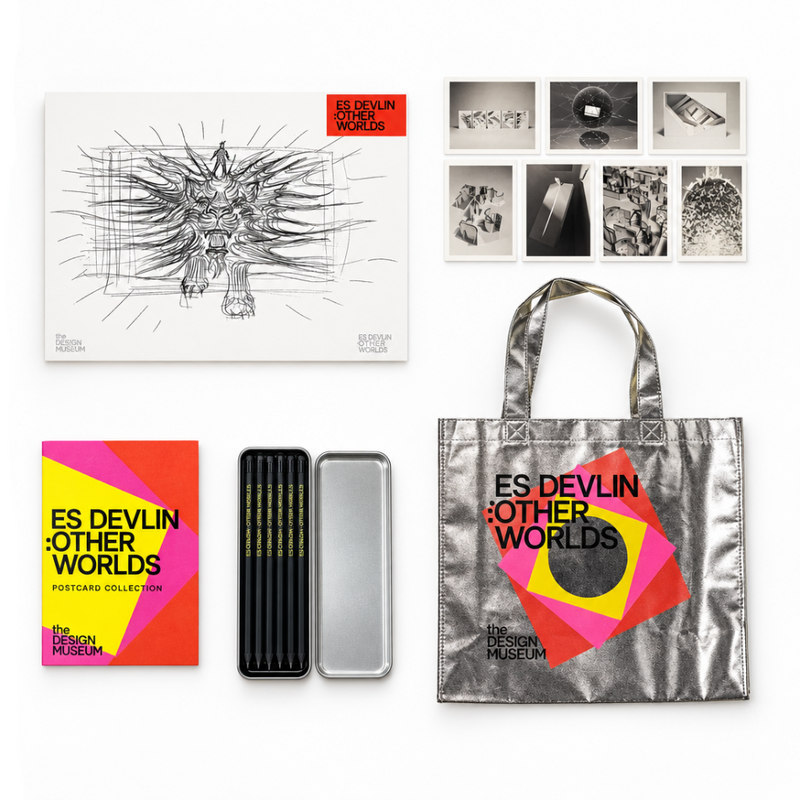 A curated flat lay of the 'Es Devlín: Other Worlds' forecastcard collection by The Design Museum, featuring a large sketch print, a metallic tote bag, a colorful booklet, a silver tin, and a row of small black-and-white photo prints on a white background.