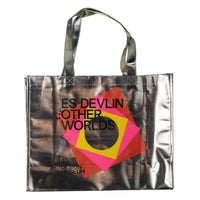 A metallic silver tote bag with black handles, featuring a colorful geometric graphic in pink, yellow, and red with the text 'ES DEVLIN OTHER WORLDS' on a pale yellow background.