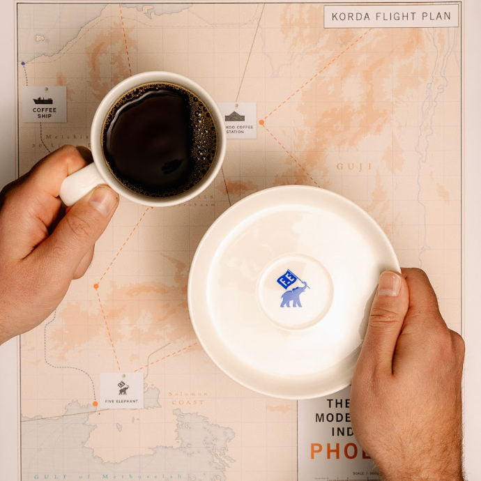 Person holding a cup of coffee with a map and 'The Phoenician Scheme' branding.