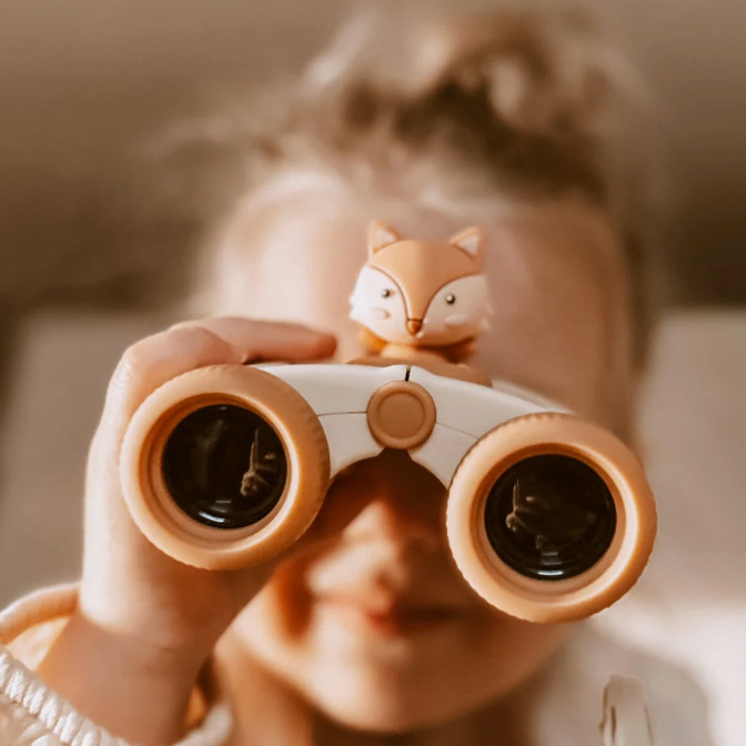Child holding toy binoculars with a fox figurine on top, against a blurred background