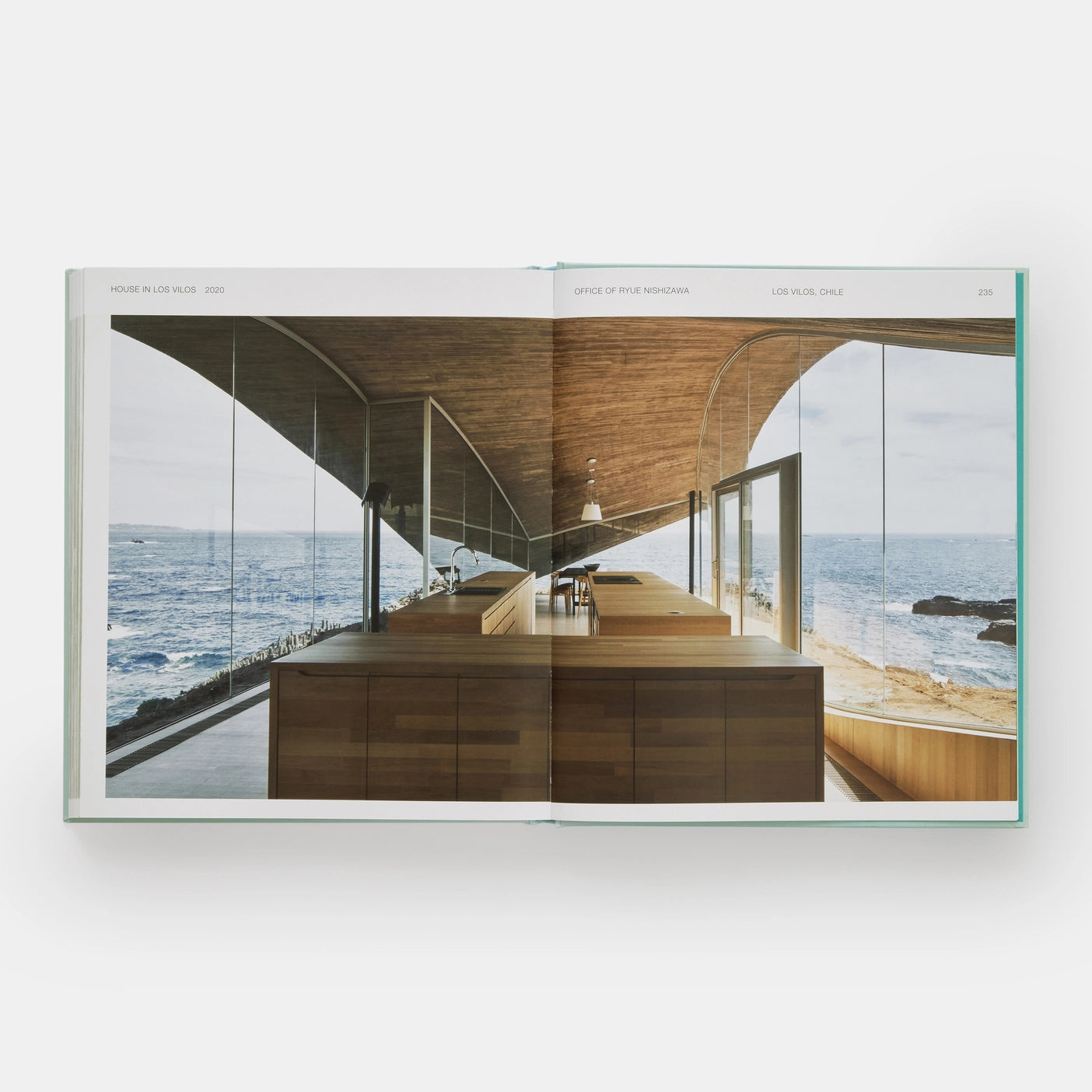 Open page of Glass Houses book featuring a photograph of a modern glass house with wooden counters amongst the sea. 