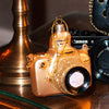 Gold camera shaped Christmas bauble on a wooden table