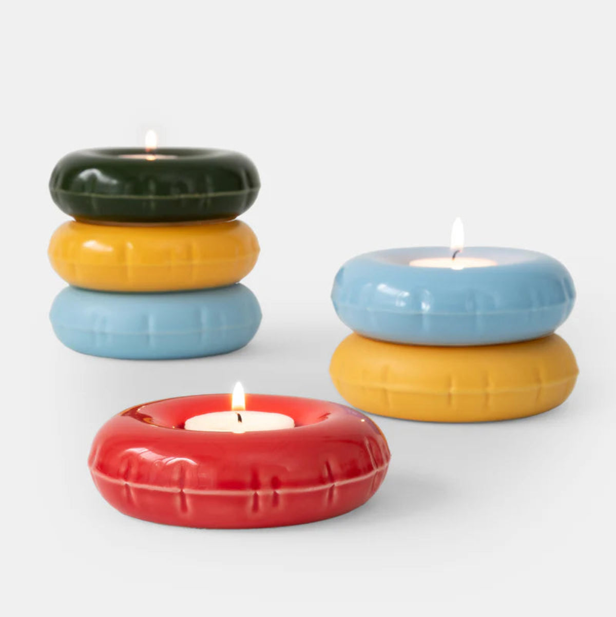 Colourful inflatable ceramic candle holders with lit candles on a white background