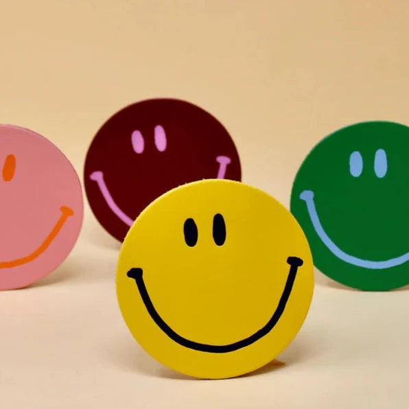 A set of four round coasters with a smiley face design. The coasters are in different colors including pink, green, yellow, and red.