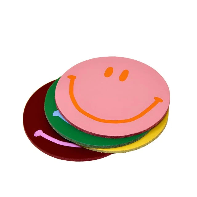 A set of four round coasters with a smiley face design, stacked in a pile. The coasters are in different colors including pink, green, yellow, and red.