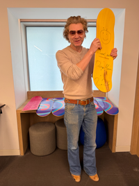 Person holding a yellow skateboard with a smiley face design in a room