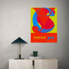 Colorful abstract poster on a wall above a wooden cabinet with a lamp and books.