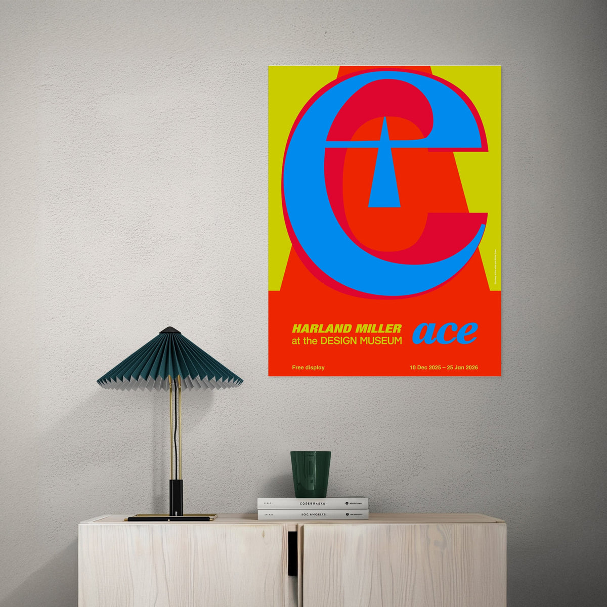 Colorful poster with geometric design on a gray wall above a wooden cabinet with a lamp and books.