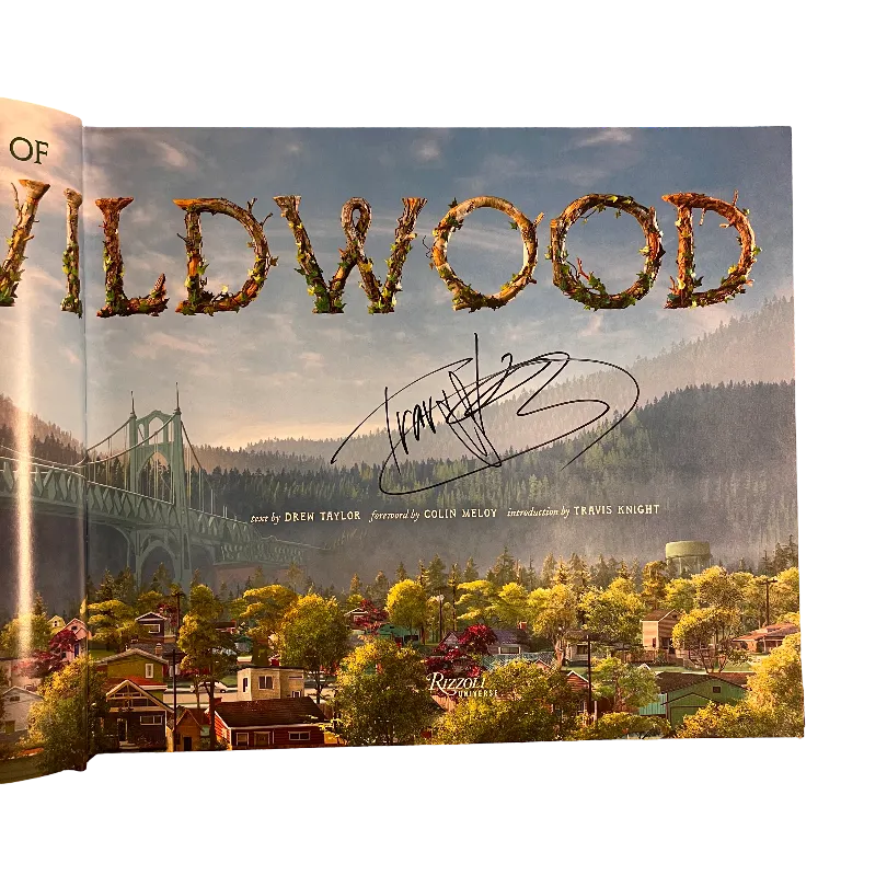 A printed book or magazine page featuring a scenic landscape with large decorative 'Wildwood' lettering across the top, a suspension bridge on the left, and a stylized town scene below. A black handwritten signature is visible near the center-right.