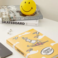 Yellow smiley face ball on a stack of books with a yellow book titled 'I Know Nigo' on a white surface.