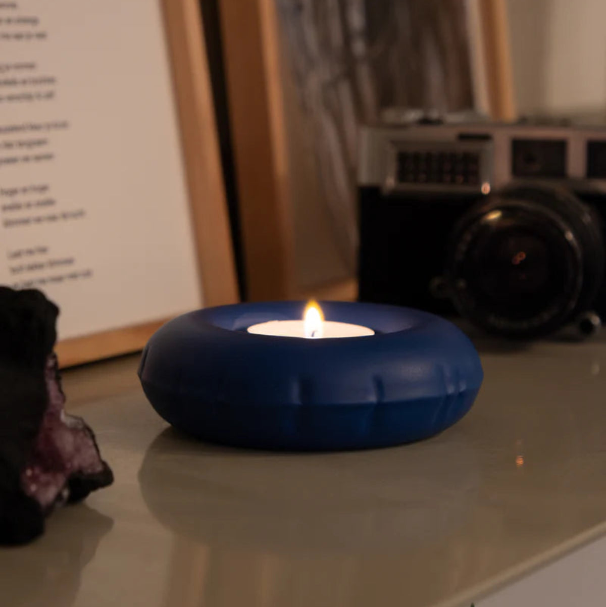 A blue inflatable ceramic candle holder with a lit candle on a table. 