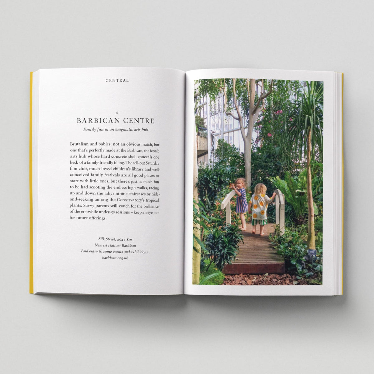 Open page of Kids London book featuring a photograph of two children on a bridge amongst lots of greenery in the Barbican Centre.