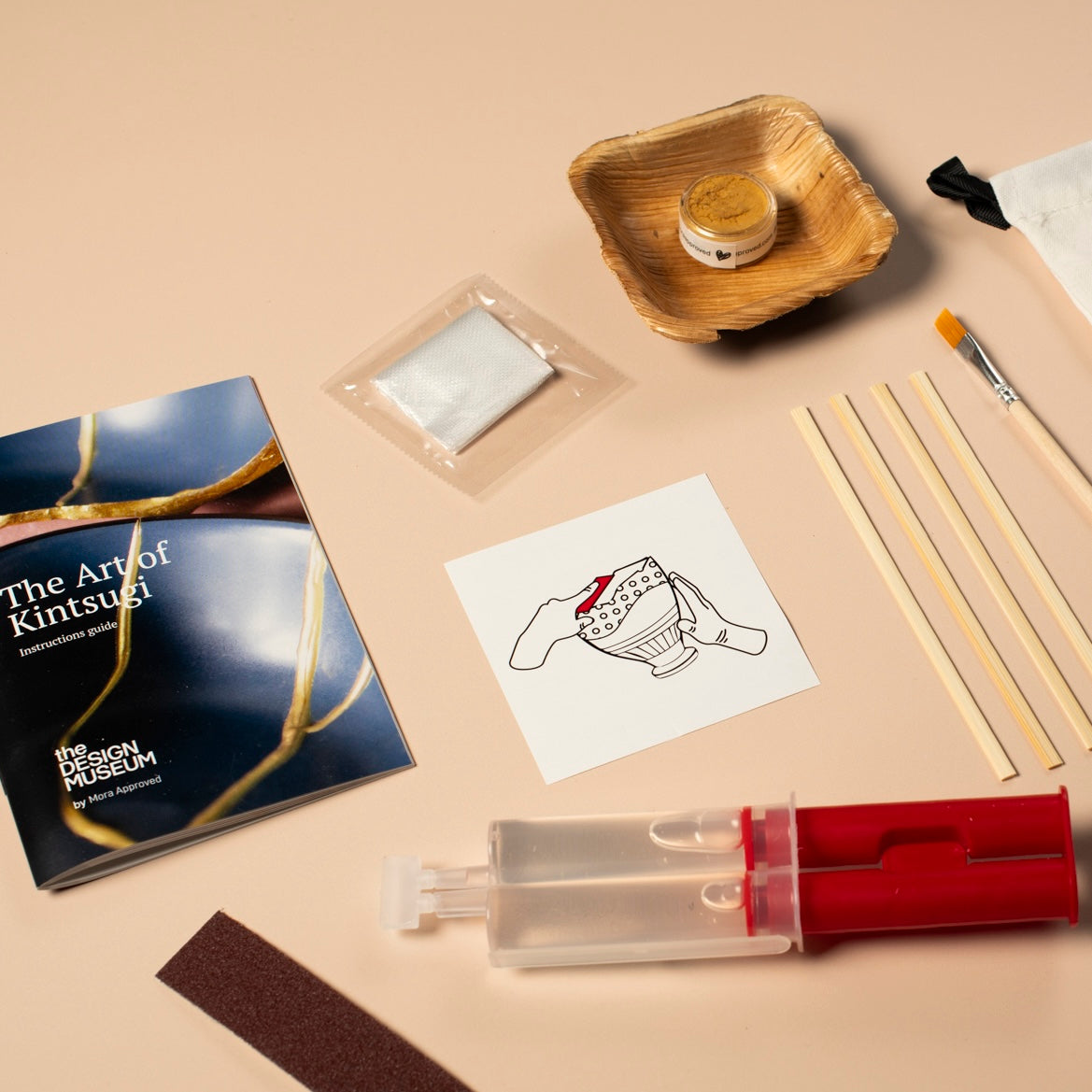 Kintsugi repair kit with tools and materials on a light pink surface.