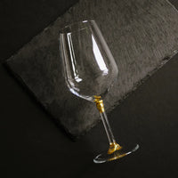 A wine glass with gold kintsugi mending  lying down on a dark grey slate.