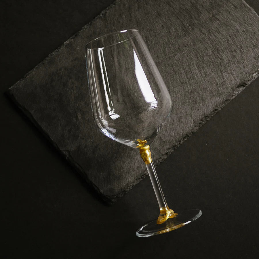 A wine glass with gold kintsugi mending  lying down on a dark grey slate.