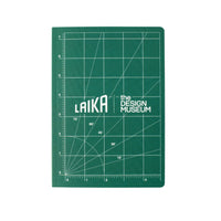 A green note book with white grid lines and the text 'LAIKA the DESIGN MUSEUM' in the center, photographed flat against a light beige background.