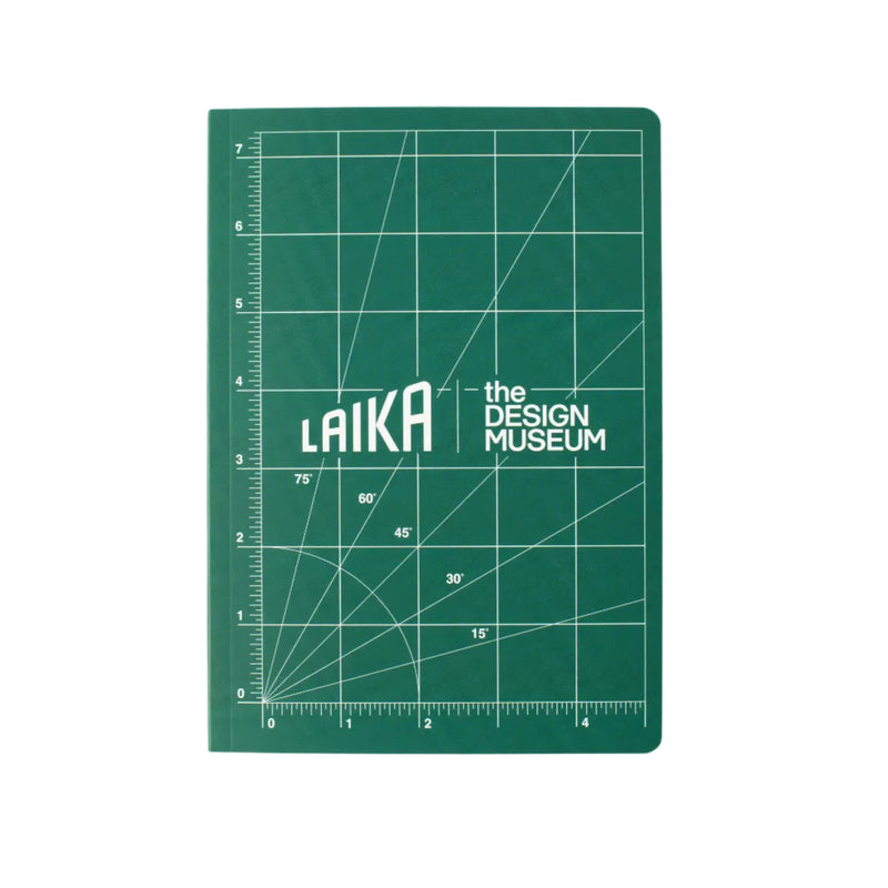 A green note book with white grid lines and the text 'LAIKA the DESIGN MUSEUM' in the center, photographed flat against a light beige background.