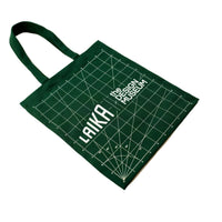 A dark green canvas tote bag with white printed grid lines and text reading 'LAIKA' and 'The Design Museum', shown on a plain white background.