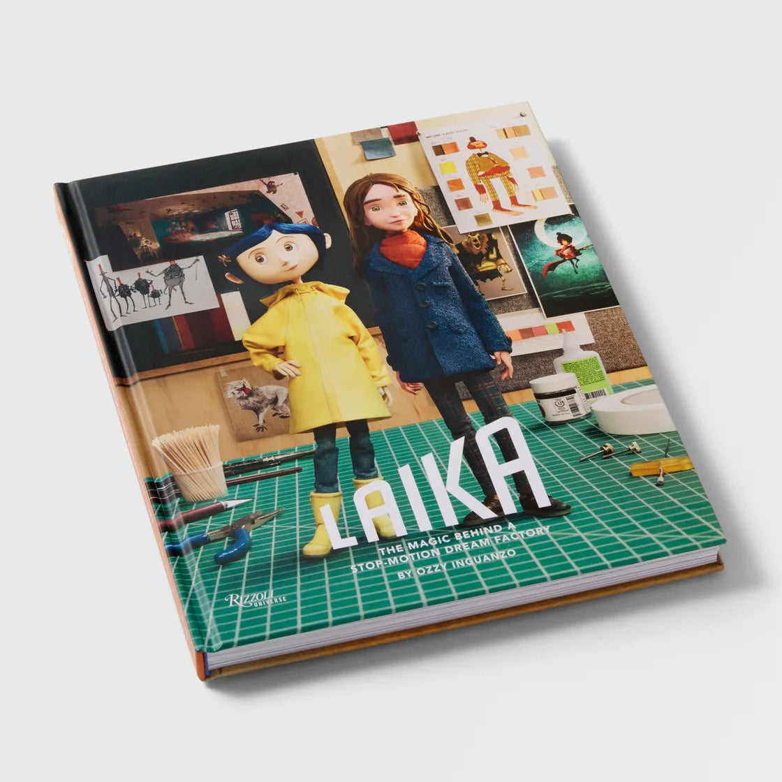 A hardcover book titled 'LAIKA' shown at an angle on a light gray background. The cover features colorful artwork of a woman and a puppet in a workshop, with a green grid floor and the title 'LAIKA' in large white letters.