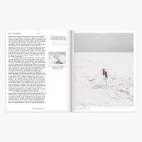 An open printed book or magazine spread laid flat on a light gray background. The left page contains black text and a small inset photo, while the right page shows a snowy outdoor scene with a person in red clothing standing in the snow.