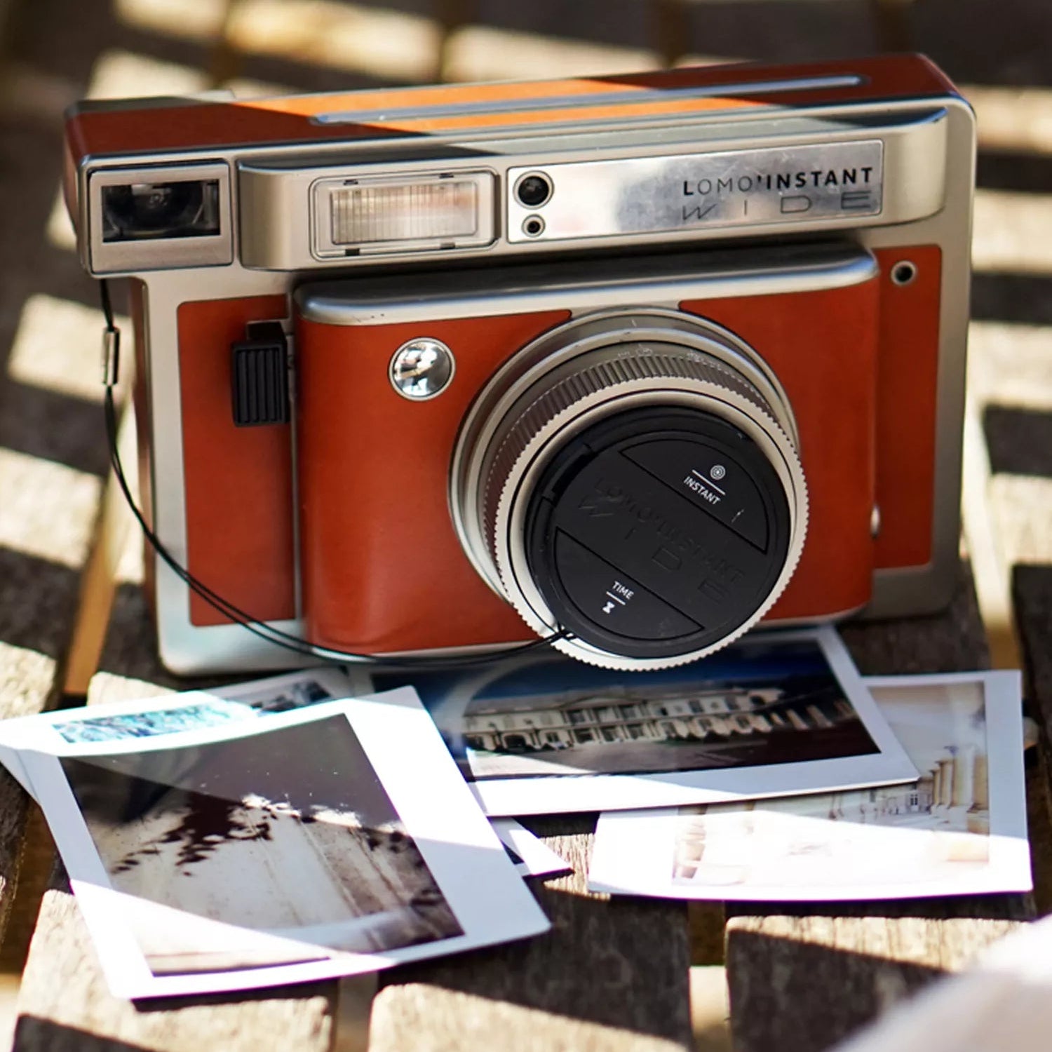 Red and silver Lomography camera with instant photos on a wooden surface