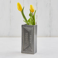 Two yellow tulips in a grey brick-shaped vase.