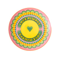 A round, hand-decorated fine bone china plate with a pink base and a heart-shaped design in the center, featuring the text 'LOVE ALWAYS' in green.