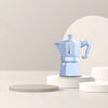 Blue espresso maker on a white pedestal against a light gray background