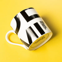 A white ceramic coffee mug with a bold black graphic print and the words 'Museum of Art' on the side, photographed on a solid yellow background.