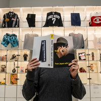 Person holding a book in front of a display of clothing and merchandise.