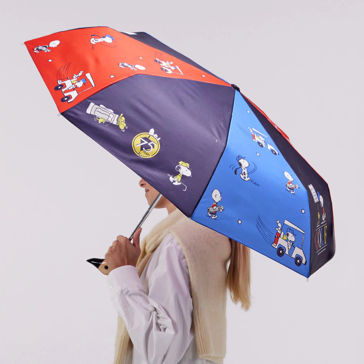 Person holding a blue and red umbrella with Snoopy pattern