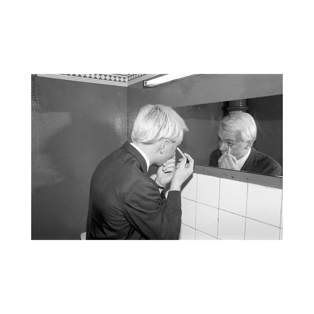 Person applying makeup in front of a mirror with tiled walls.