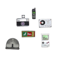 Set of vintage-themed pins featuring a camera, phone, cassette tape, and game console on a white background.