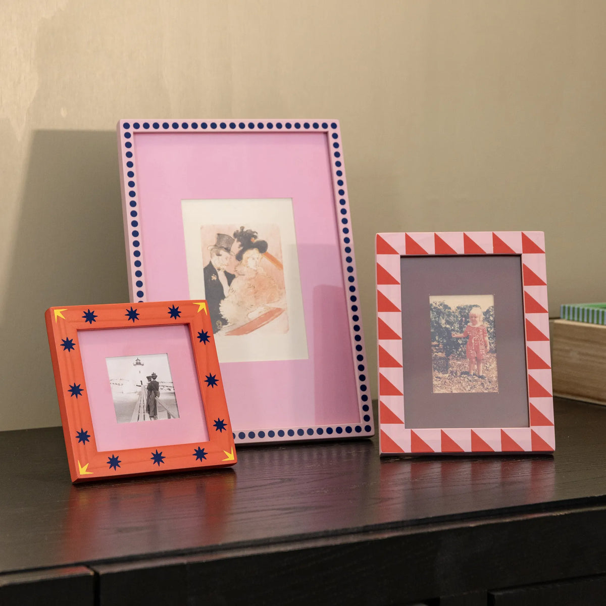 Three colourful pink photo frames on a wooden surface against a beige wall