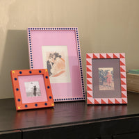Three colourful pink photo frames on a wooden surface against a beige wall