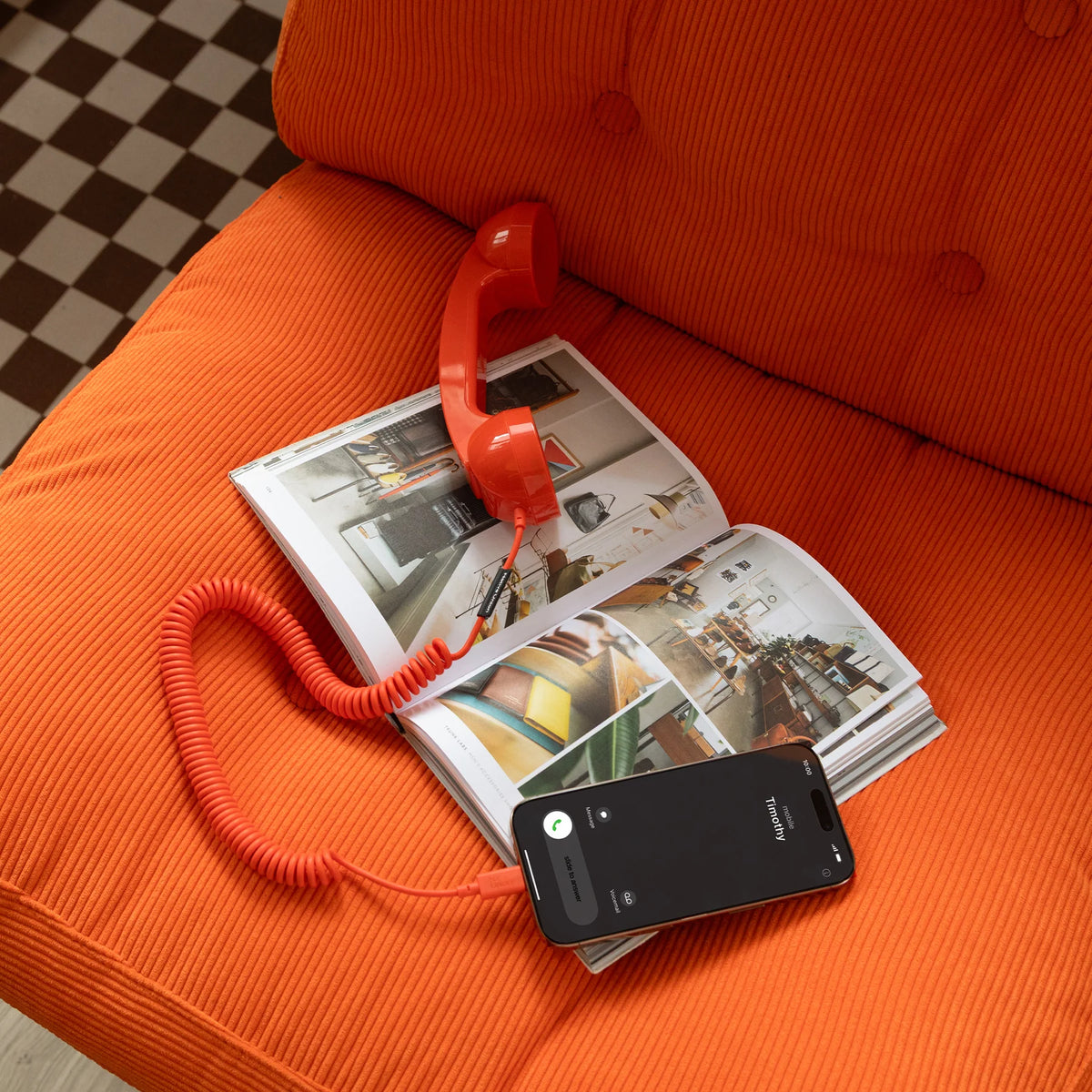 Red toy phone on an open magazine with a smartphone on an orange couch.