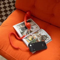 Red toy phone on an open magazine with a smartphone on an orange couch.