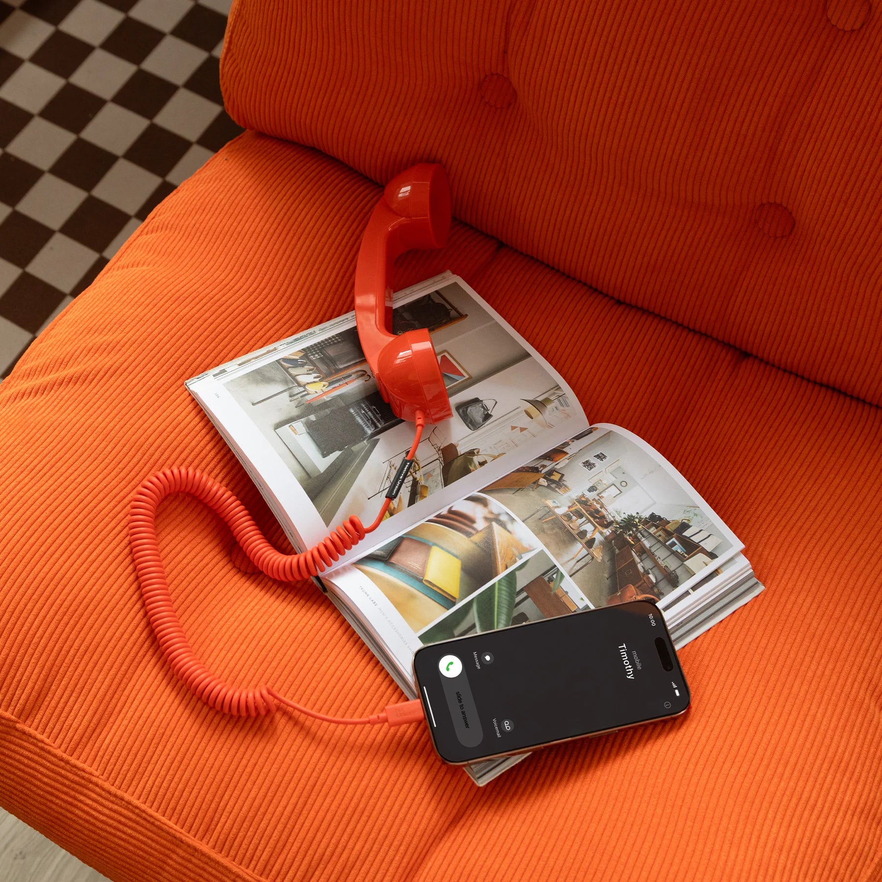 Red toy phone on an open magazine with a smartphone on an orange couch.