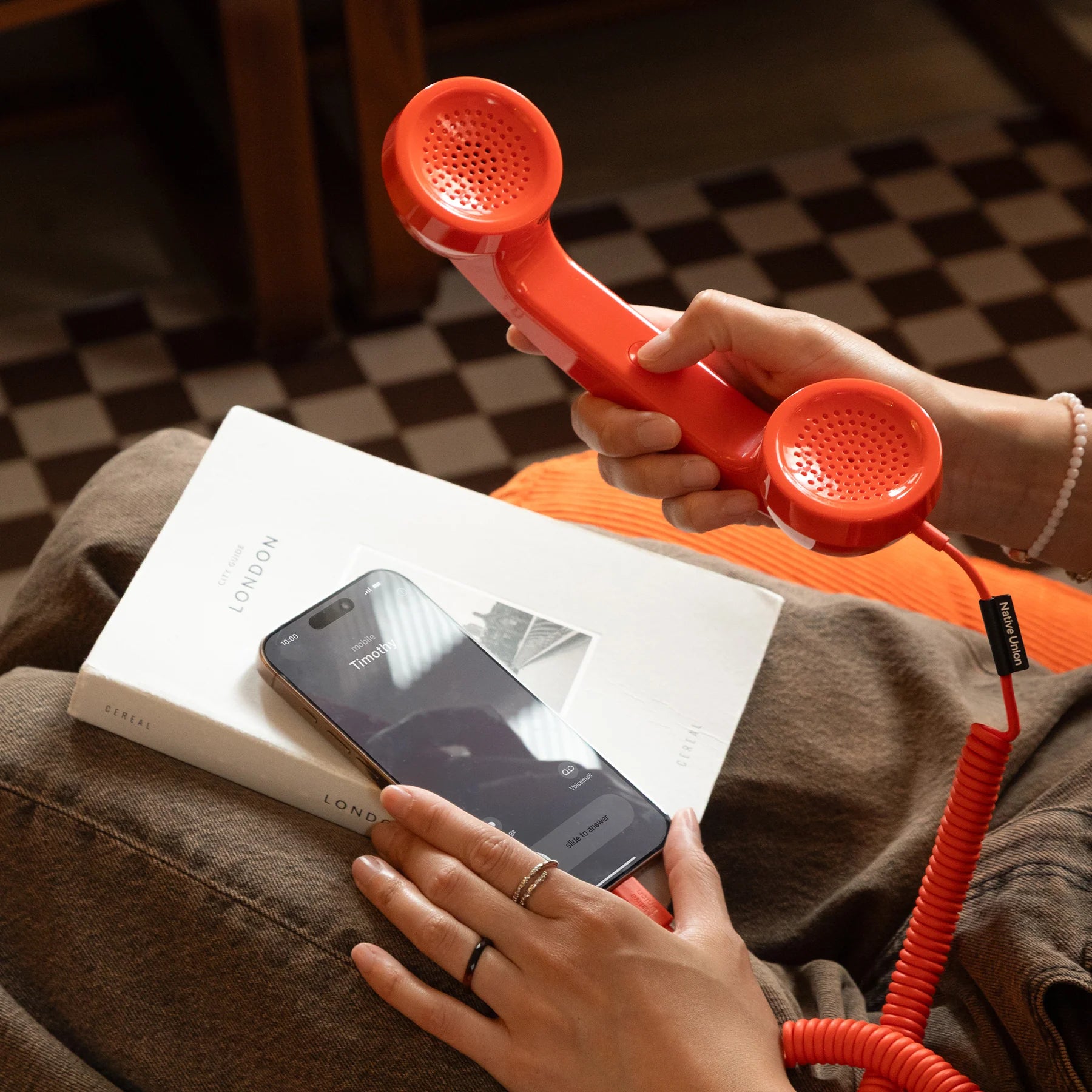 Person holding a red retro-style phone handset over a smartphone on a book.