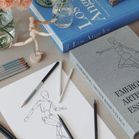 Artistic setup with books, pencils, and a drawing of a figure on a table.