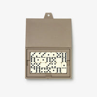 An open rectangular domino box in taupe leather, displaying a set of cream and black domino tiles arranged inside, photographed on a clean white background.