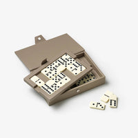 A compact domino game set in a taupe-brown leather case, shown open with domino tiles sliding out and a few loose dominoes on a clean white background.