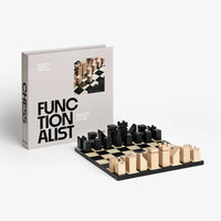 A modern chess set with minimalist wooden pieces in black and natural wood, displayed next to its white book-style box