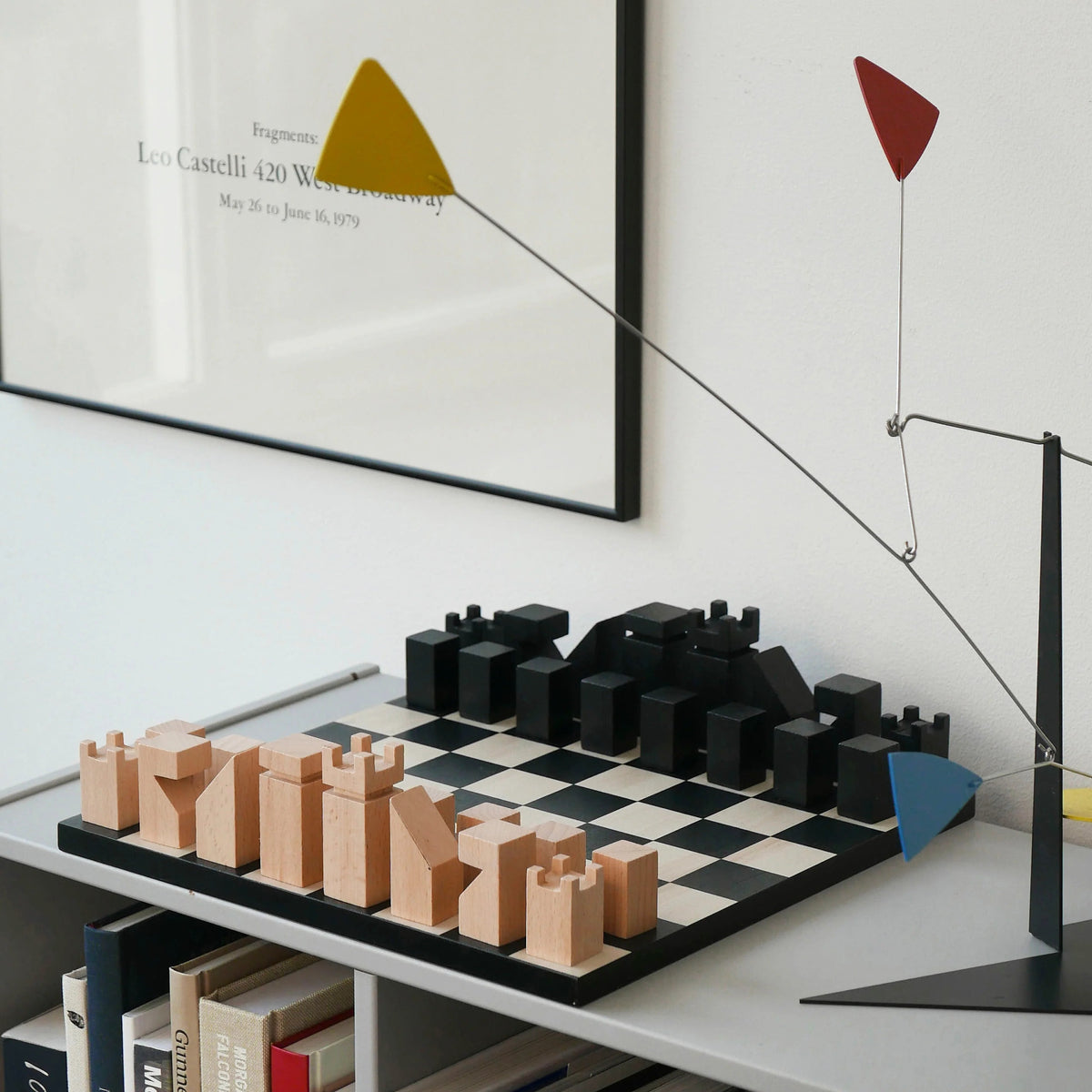 A modern minimalist wooden chess board on a shelf, with a framed print on a white wall.