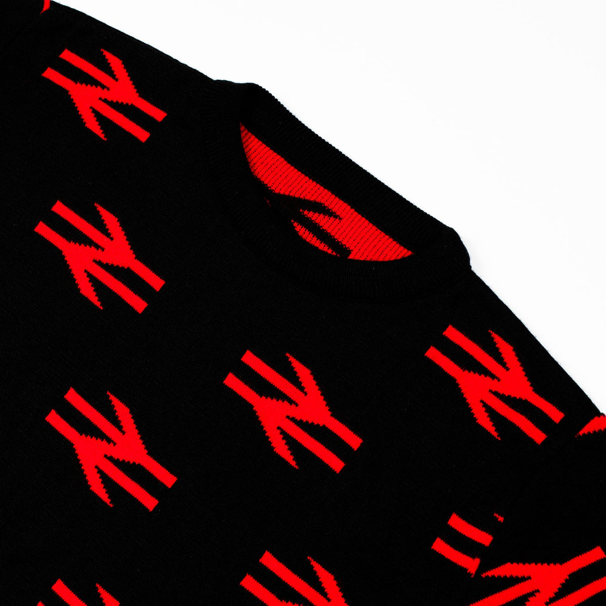 Close-up of a black knit sweater featuring a repeating red knit rail logo pattern, shown against a plain white background.